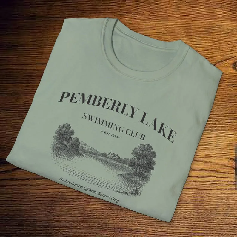 Folded sage green t-shirt on wooden background, Pemberley Lake Swimming Club design centered.