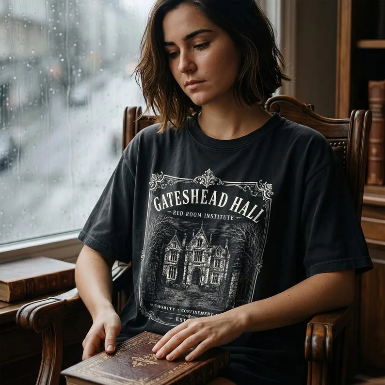 Black Comfort Colors Jane Eyre Gateshead Hall t-shirt worn by a woman at a gothic window in a dark academia setting