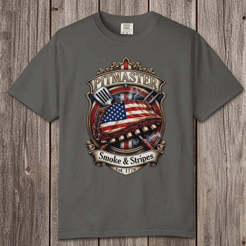 Front view of a Pepper gray Comfort Colors 1717 t-shirt laid flat on a weathered vertical wood plank background, featuring a highly detailed vintage Pitmaster American flag ribs graphic badge.