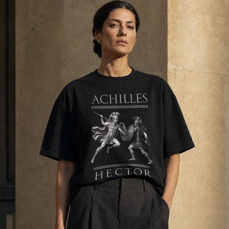 Woman wearing a black Comfort Colors T-shirt featuring an engraved Achilles and Hector battle design.